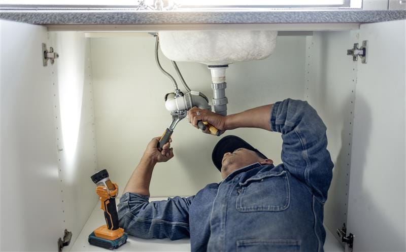 Plumber repairing pipes beneath a bathroom sink in Beverly Hills